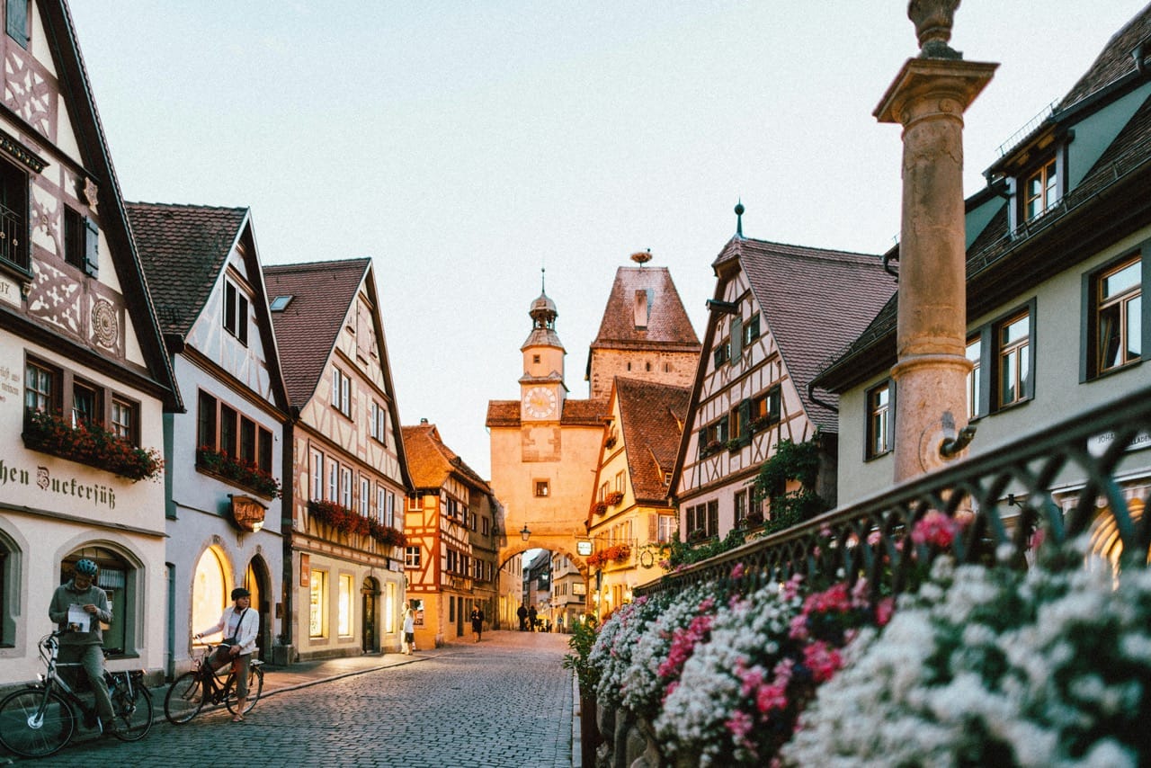 Rue pittoresque dans la ville médiévale de Rothenburg ob der Tauber, Allemagne, avec maisons à colombages, fleurs décoratives et tour d’horloge en arrière-plan.