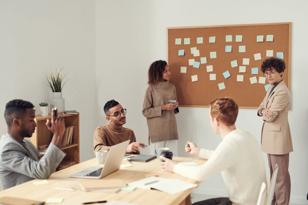 Séance de brainstorming en équipe dans une salle de réunion, avec un tableau couvert de post-it colorés et plusieurs collègues échangeant idées et stratégies autour d’une table.