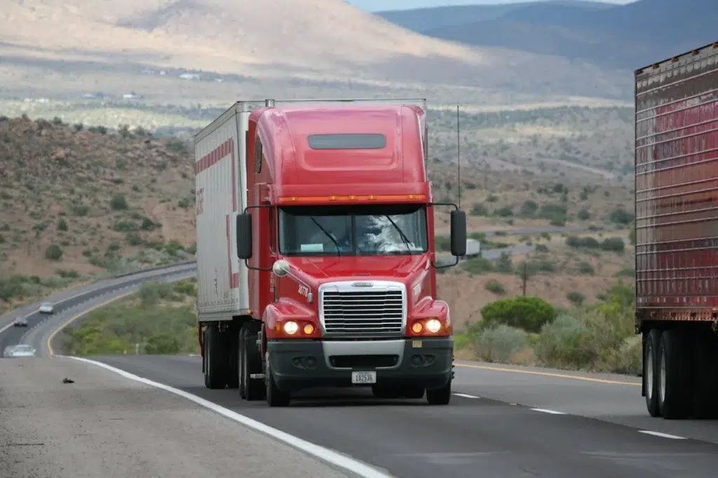 Poids lourd rouge circulant sur une route de montagne, dans un environnement semi-aride, croisant un autre camion sur la voie opposée.