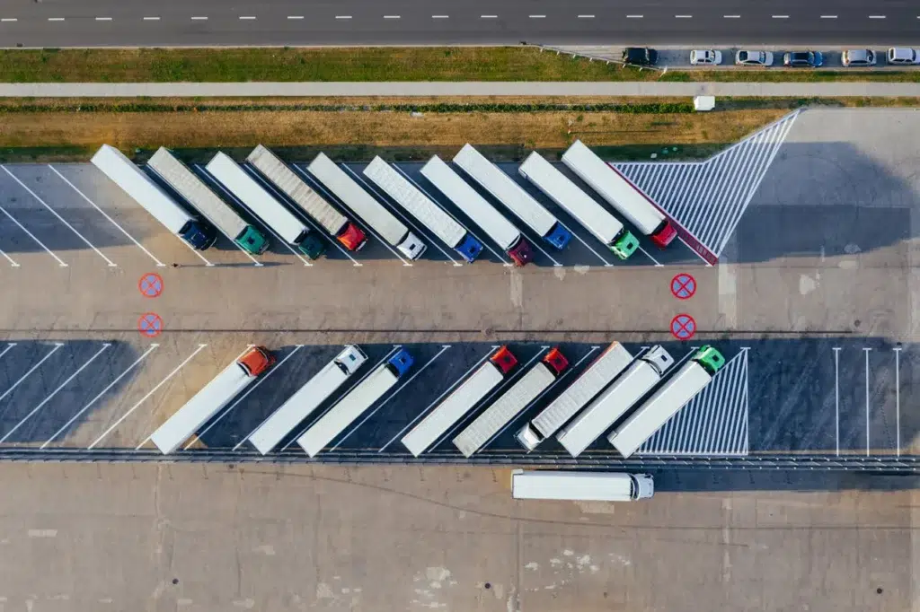 Vue aérienne d’un parking poids lourds bien organisé, avec des camions stationnés en diagonale sur des emplacements dédiés, près d’une route principale.