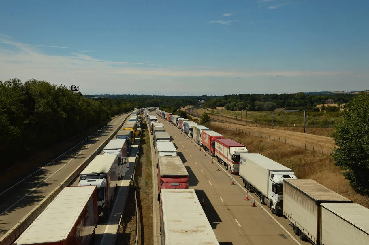 Vue aérienne d’une file ininterrompue de camions à l’arrêt sur une autoroute, déviés sur une seule voie, dans un paysage rural sous ciel dégagé.