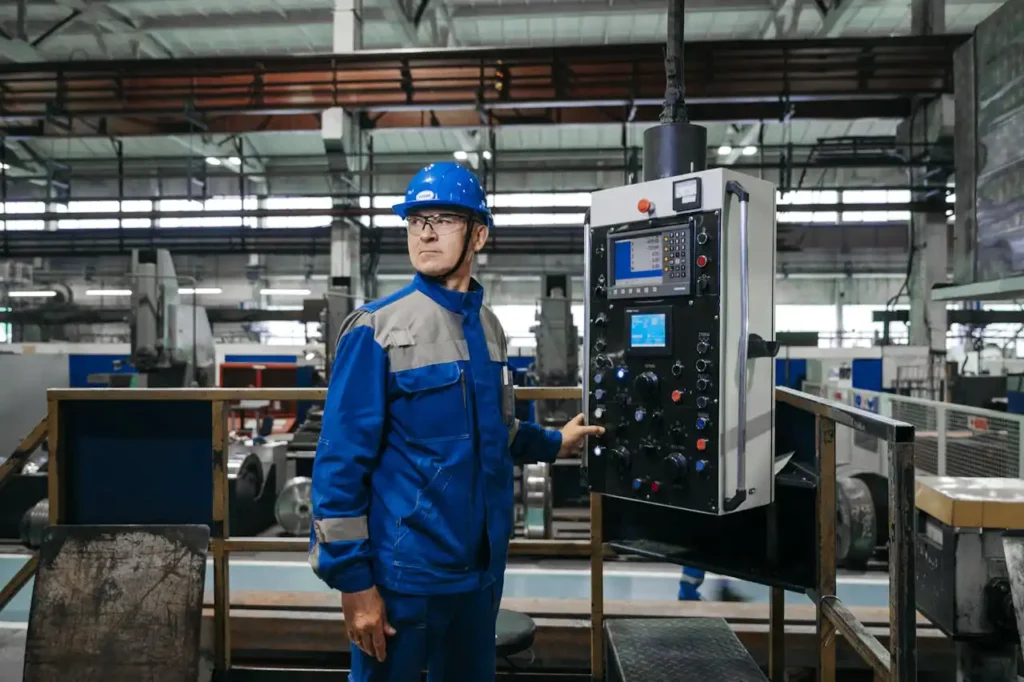 Ouvrier en tenue de protection bleue et casque de sécurité bleu, utilisant un panneau de commande industriel dans une usine de production.