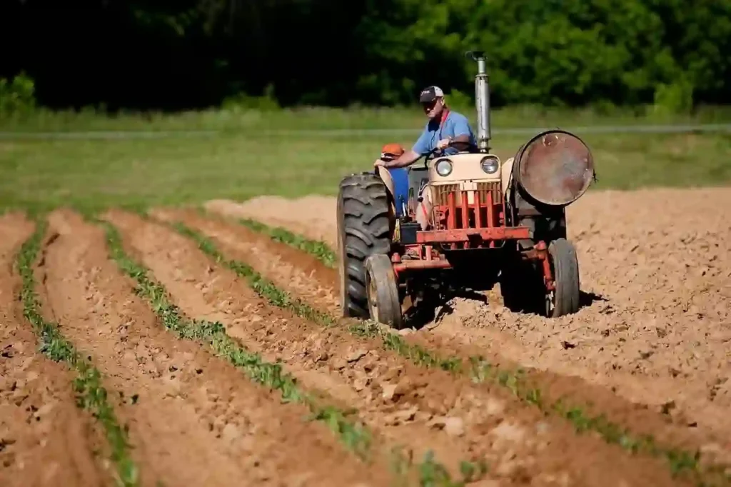 Agriculteur conduisant un tracteur rouge dans un champ labouré, en train de travailler la terre.
