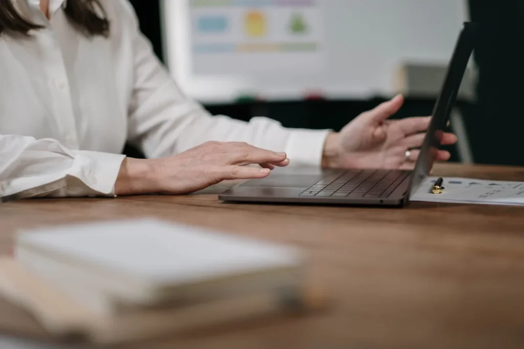 Personne travaillant sur un ordinateur portable, avec des documents posés sur un bureau en bois.
