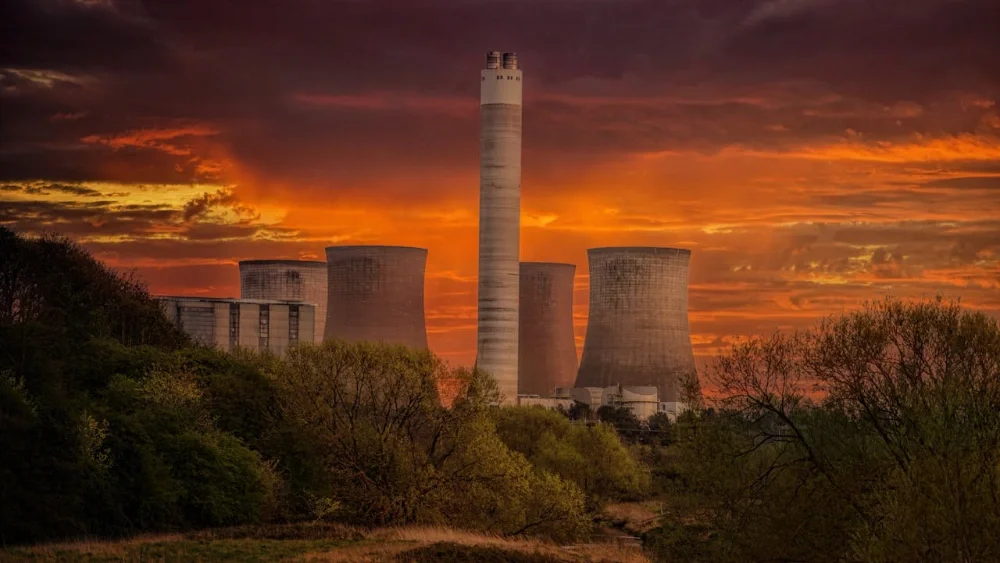 Centrale industrielle avec plusieurs tours de refroidissement, photographiée au coucher du soleil avec un ciel orange dramatique.