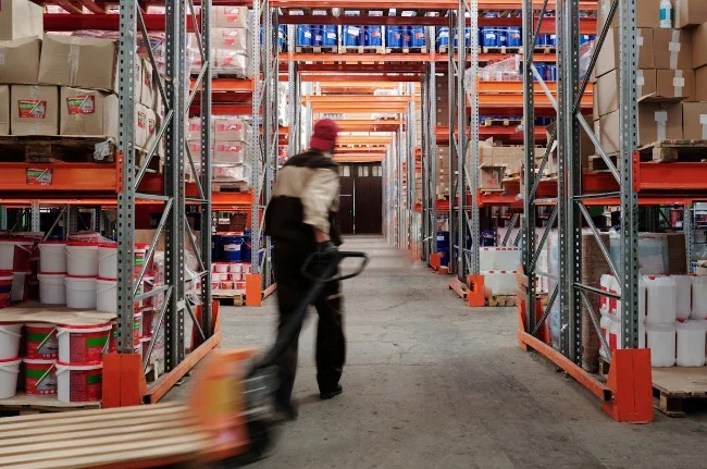 Ouvrier manipulant un transpalette manuel dans l’allée d’un entrepôt logistique.