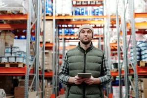 Responsable logistique tenant une tablette numérique au milieu d’un entrepôt de stockage.
