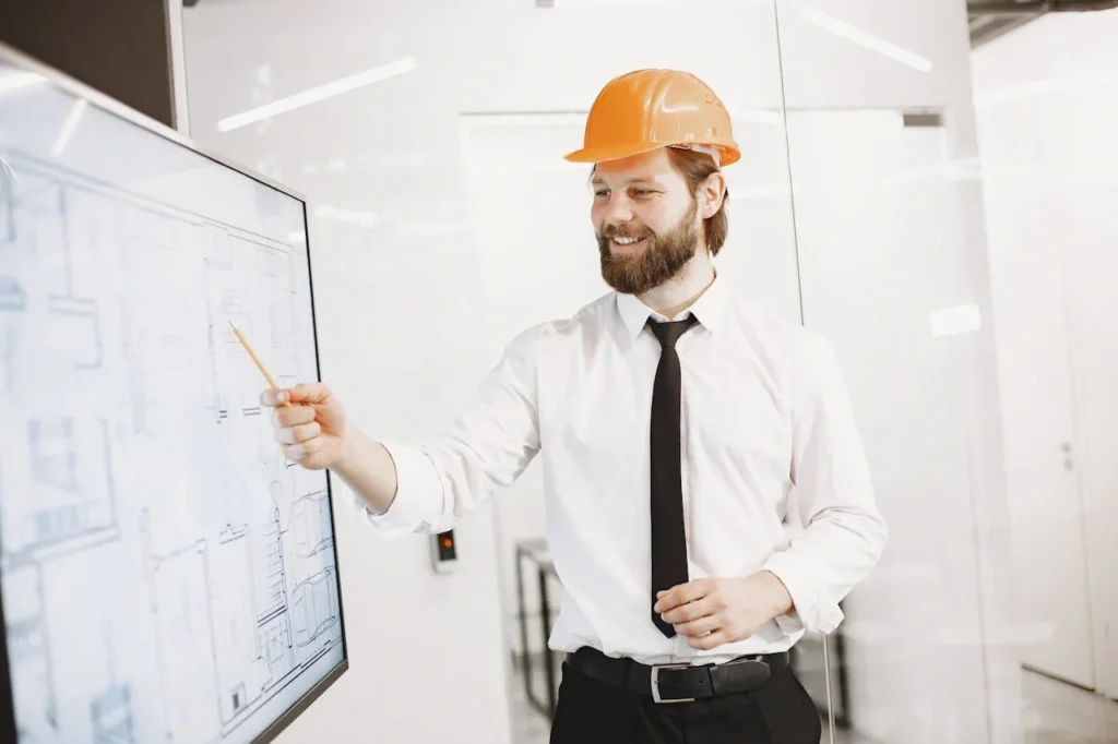 Ingénieur portant un casque de chantier présentant des plans techniques sur un écran numérique.