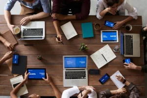 Vue aérienne d’une réunion d’équipe avec ordinateurs portables, tablettes et carnets sur une table de travail.