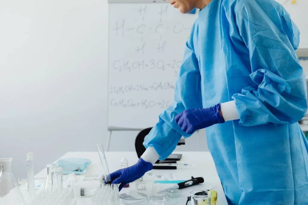 Professionnel de laboratoire manipulant des tubes à essai et des échantillons sur une paillasse, portant des gants et une tenue de protection.