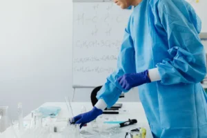 Professionnel de laboratoire manipulant des tubes à essai et des échantillons sur une paillasse, portant des gants et une tenue de protection.