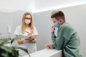 Professionnelle de santé portant un masque échange avec un patient dans un cabinet médical.