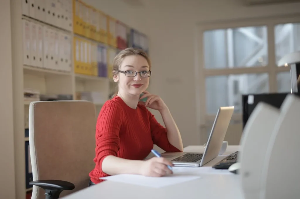 Femme travaillant seule dans un bureau, assise à son poste avec un ordinateur portable et des documents administratifs.